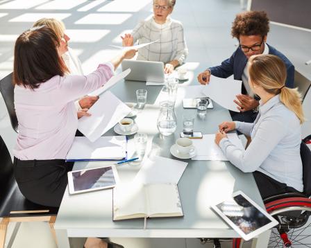 A diverse group of adults work at a table together.
